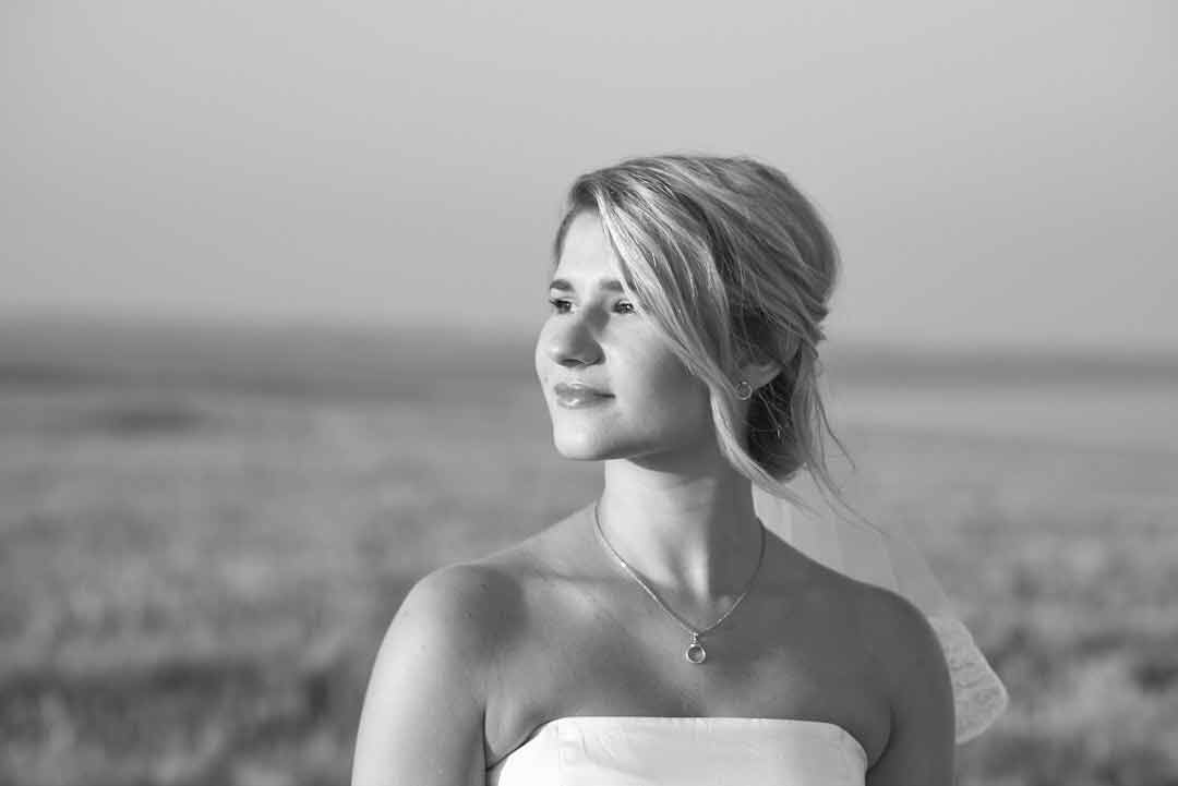 Black and white portrait of smiling bride wearing a strapless white wedding dress looking towards the sun during golden hour.