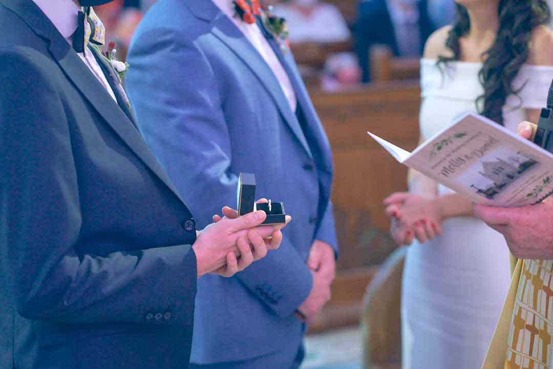 Best man holds wedding ring in the box at the church alter. Bride and groom can be seen standing behind him