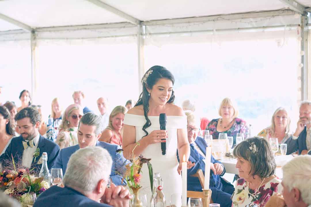 Bride holding the microphone thanking her mom during the wedding speeches. The venue is a white big white tent.