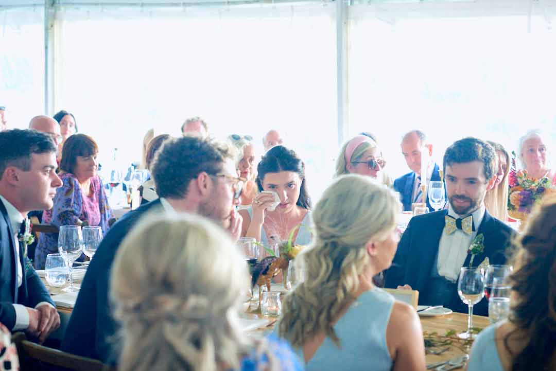 Wedding guest wiping a tear from her eye with a tissue during the wedding speeches.