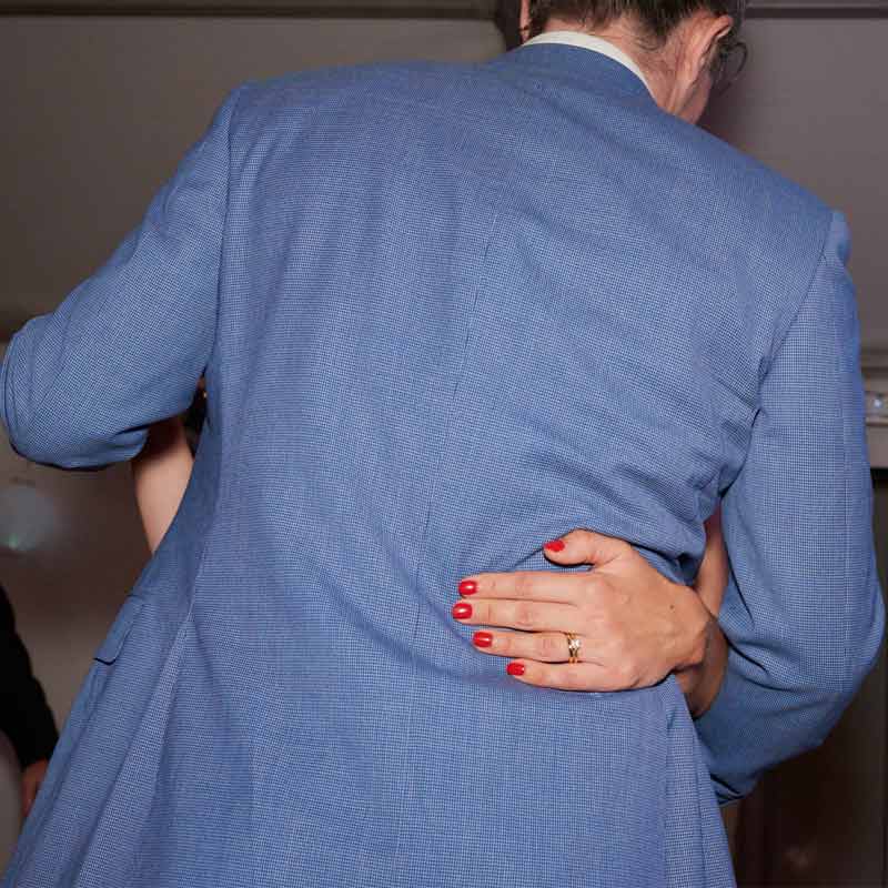 Back of the grooms blue jacket as he dances with the bride during the first dance. We can see the left hand of the bride wrap around his waist with bright red nail polish and her wedding ring.